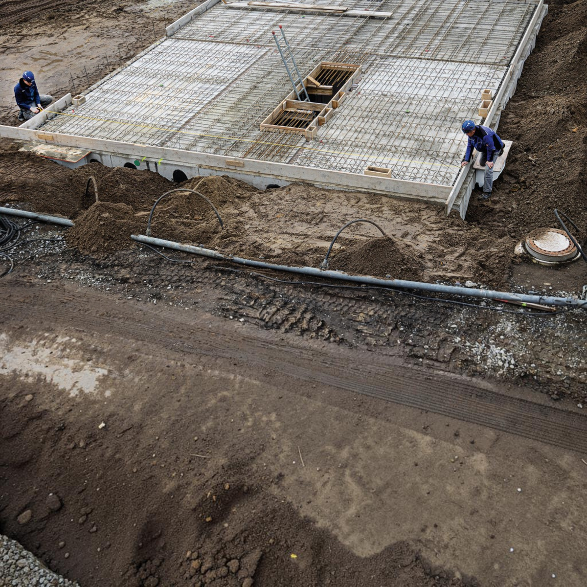 Zwei Bauarbeiter nutzen das Werkfit Kapselbandmaß LBM 2000 STEEL zur Vermessung einer Betonfundamentplatte auf Baustelle