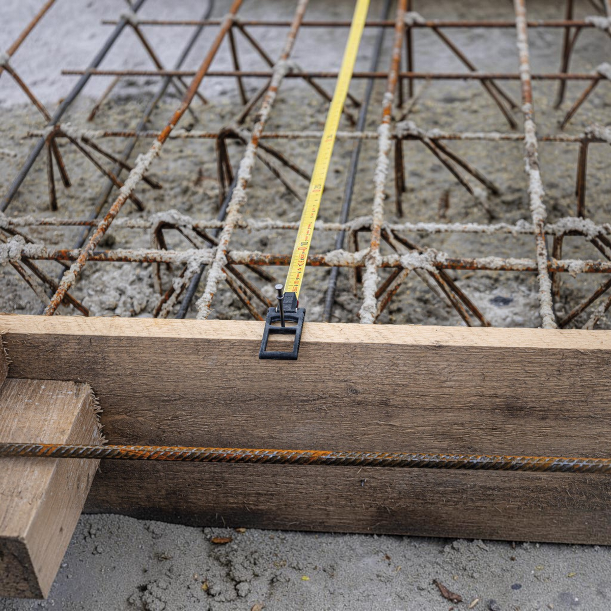 Werkfit Kapselbandmaß LBM 2000 STEEL aus gelbem Stahl auf einer Baustelle mit Bewehrungsstahl und Holzschalung