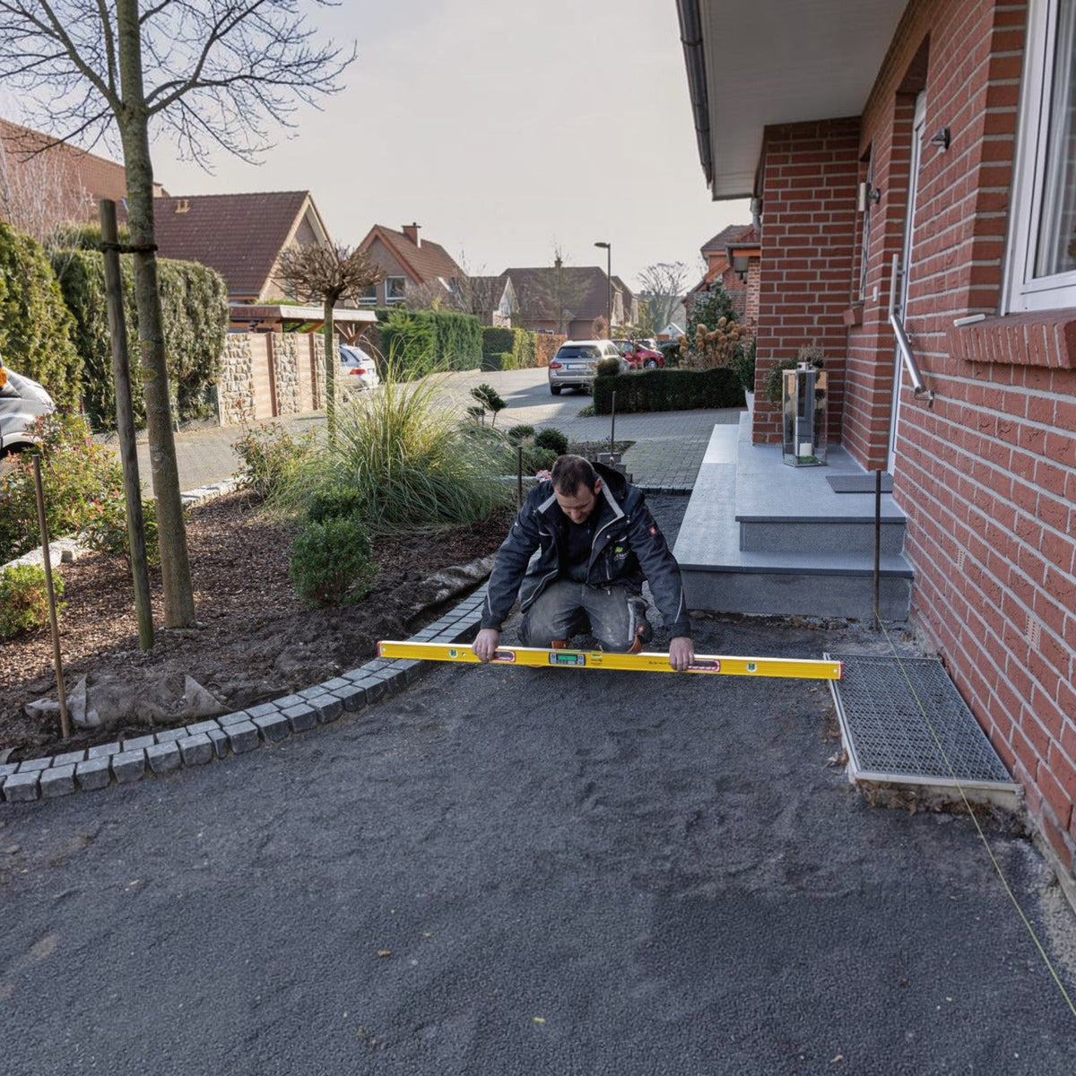 Werkfit Elektronik-Wasserwaage TECH 196 DL im Einsatz bei Pflasterarbeiten vor einem Wohnhaus