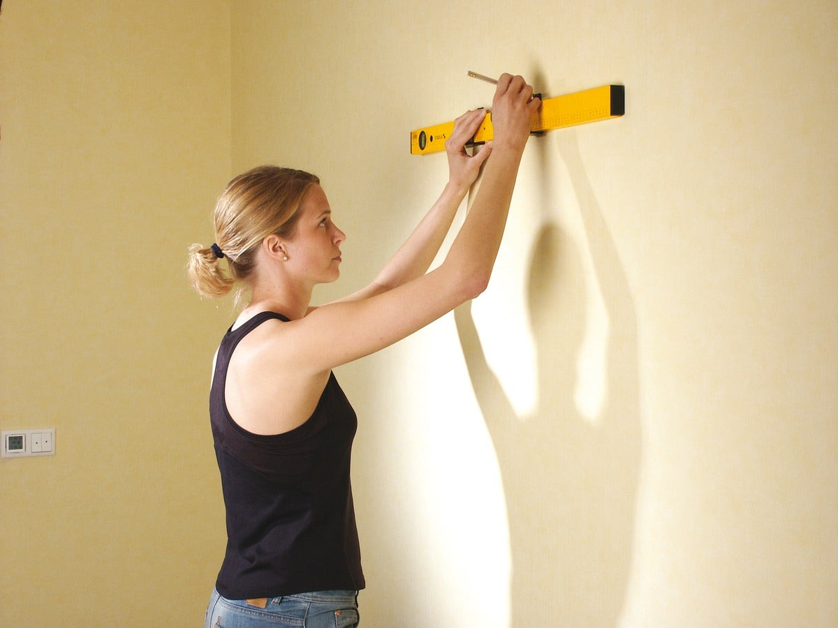 Eine Frau benutzt eine gelbe Werkfit Wasserwaage Type 70 MAS 80 cm, um eine Markierung an einer Wand zu setzen.
