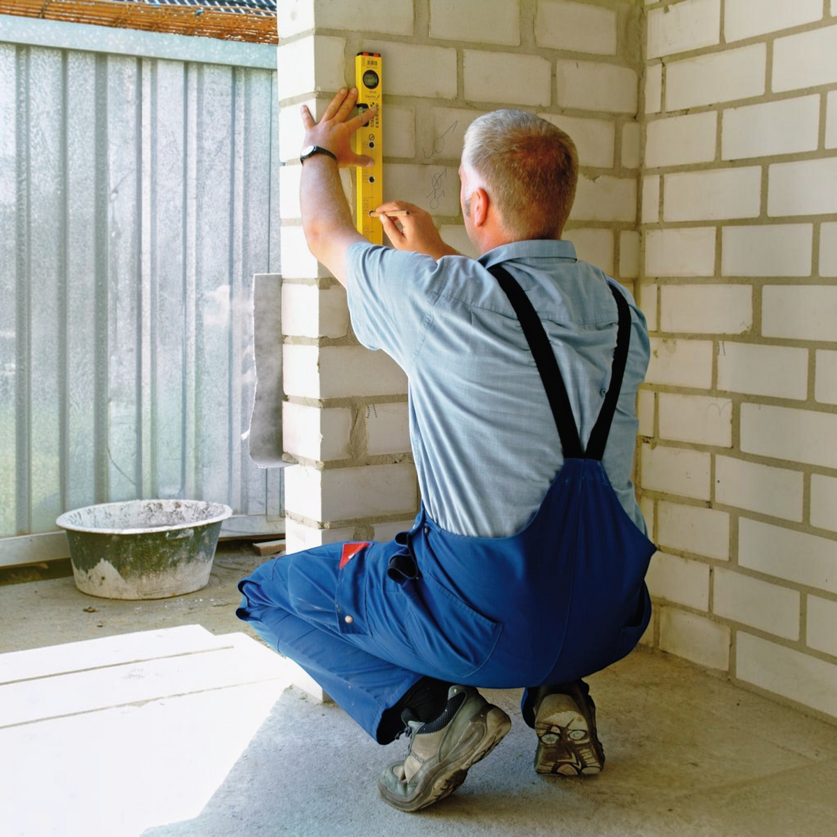 Handwerker von Werkfit nutzt eine gelbe Wasserwaage Type 70 Electric zum Anzeichnen an einer hellen Ziegelwand