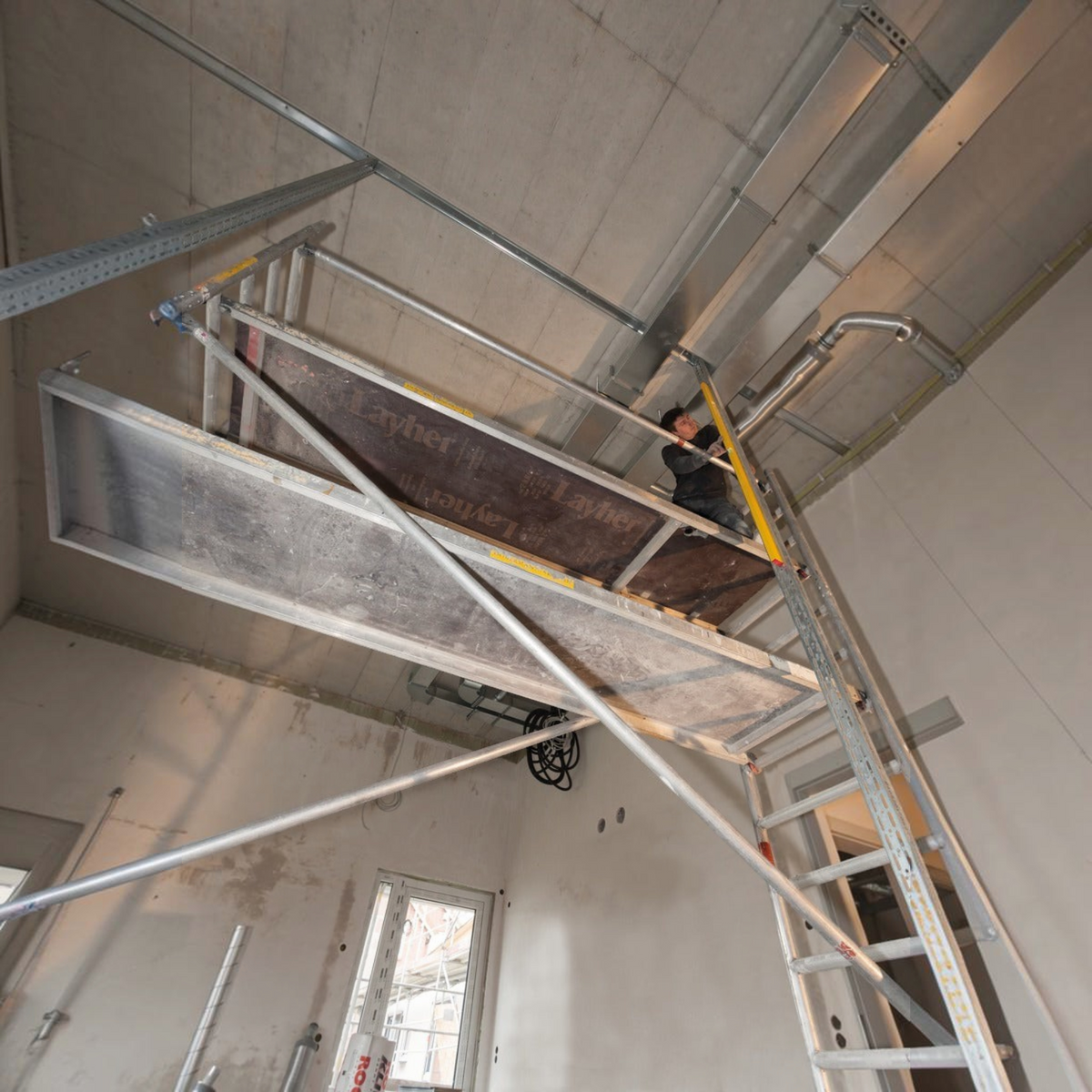 Handwerker verwendet Werkfit Wasserwaage Type 80 ASM auf einem Layher Gerüst bei der Deckenmontage